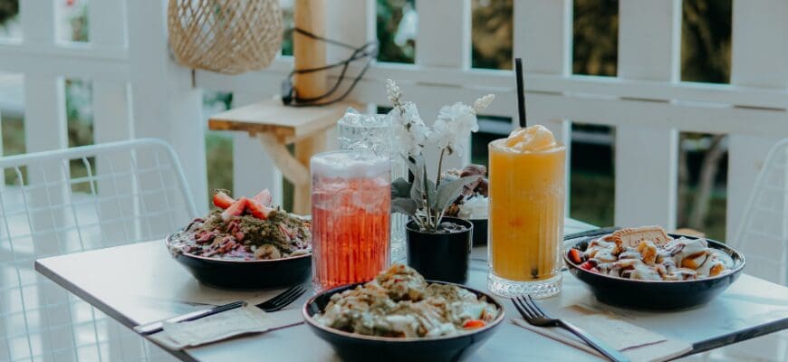 Outdoor patio table at a cafe with three bowls of food and two iced drinks