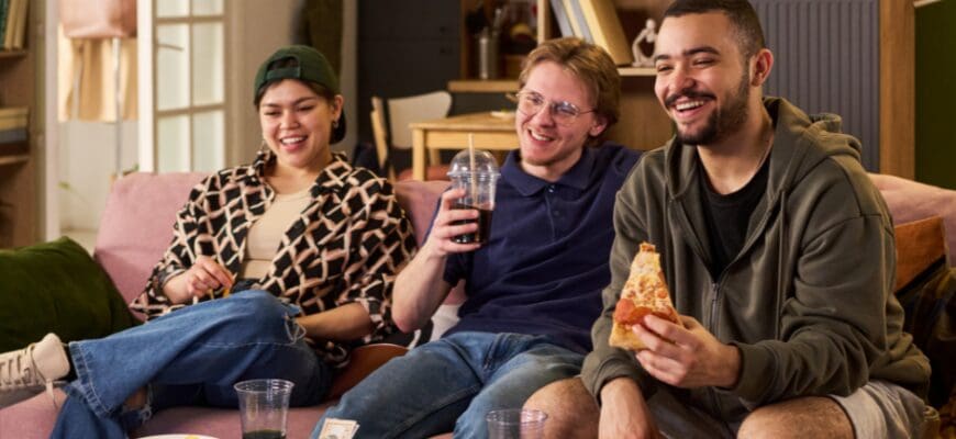 Three friends sharing a pizza and sitting on an apartment living room couch